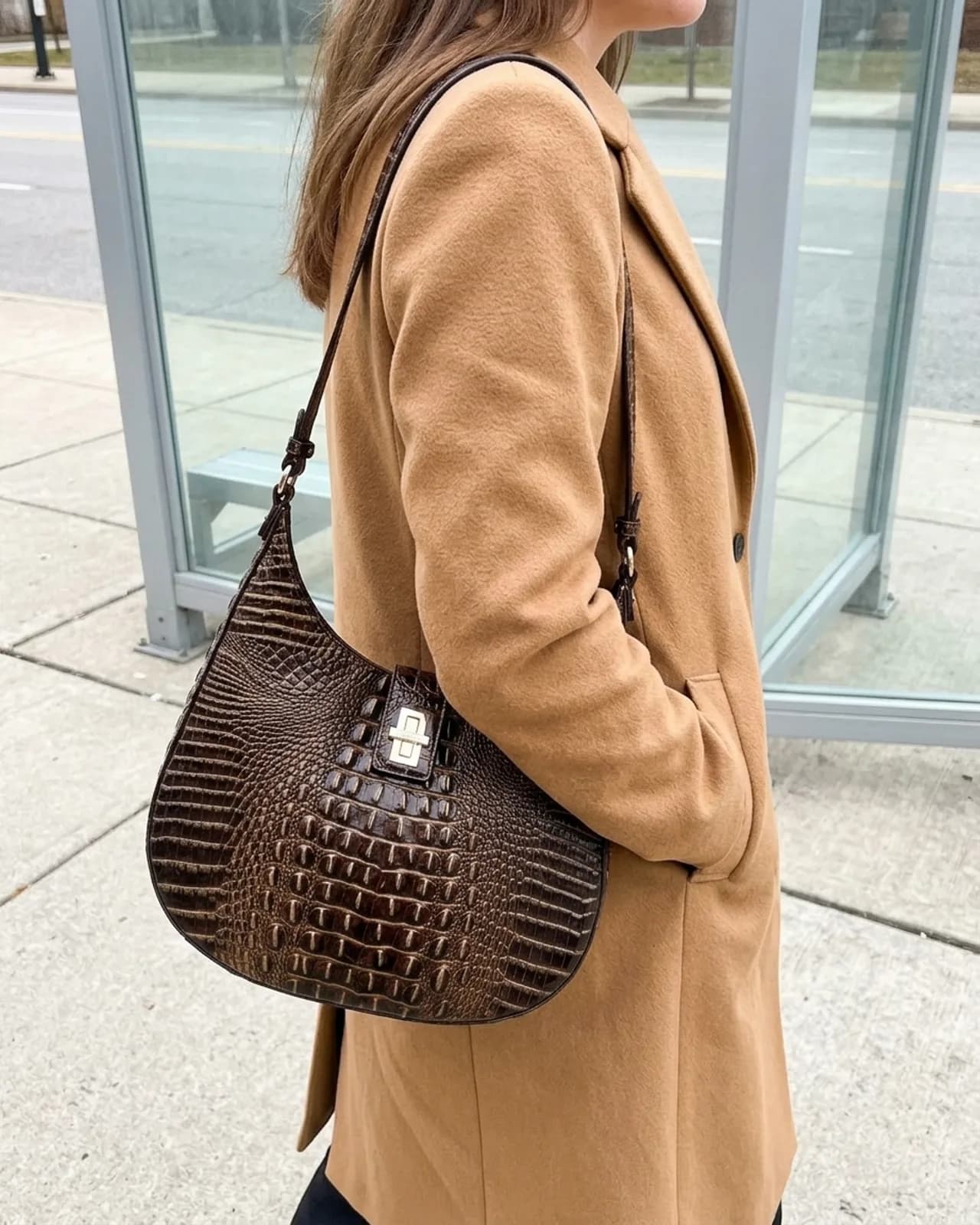 Brahmin Fallon croc-embossed leather shoulder bag hanging from the shoulder of a camel coat on a city pavement